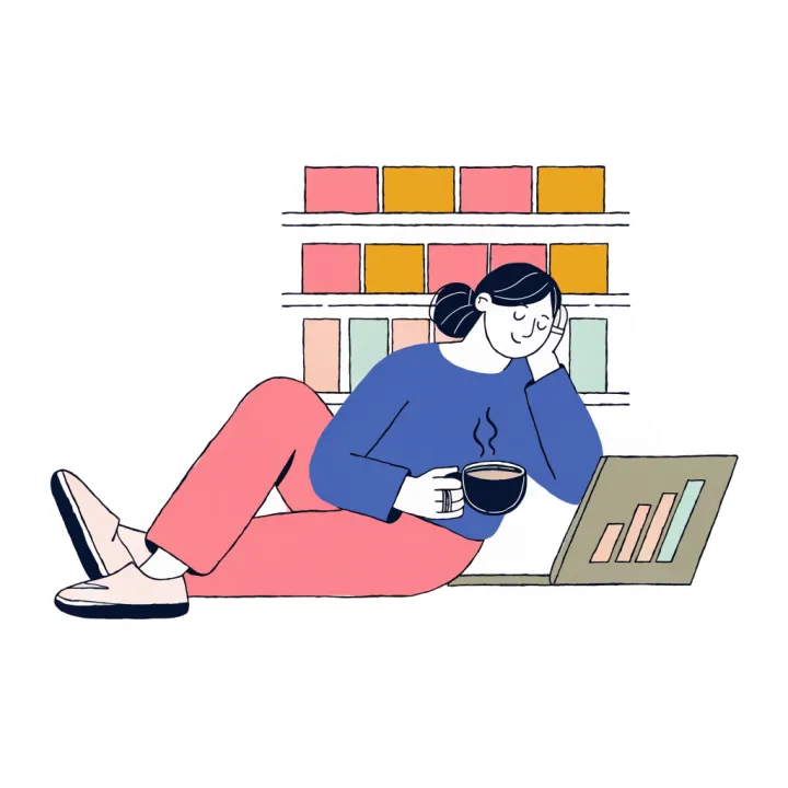 A seller relaxing with a cup of chai beside her laptop, neat shelves of stock behind her.